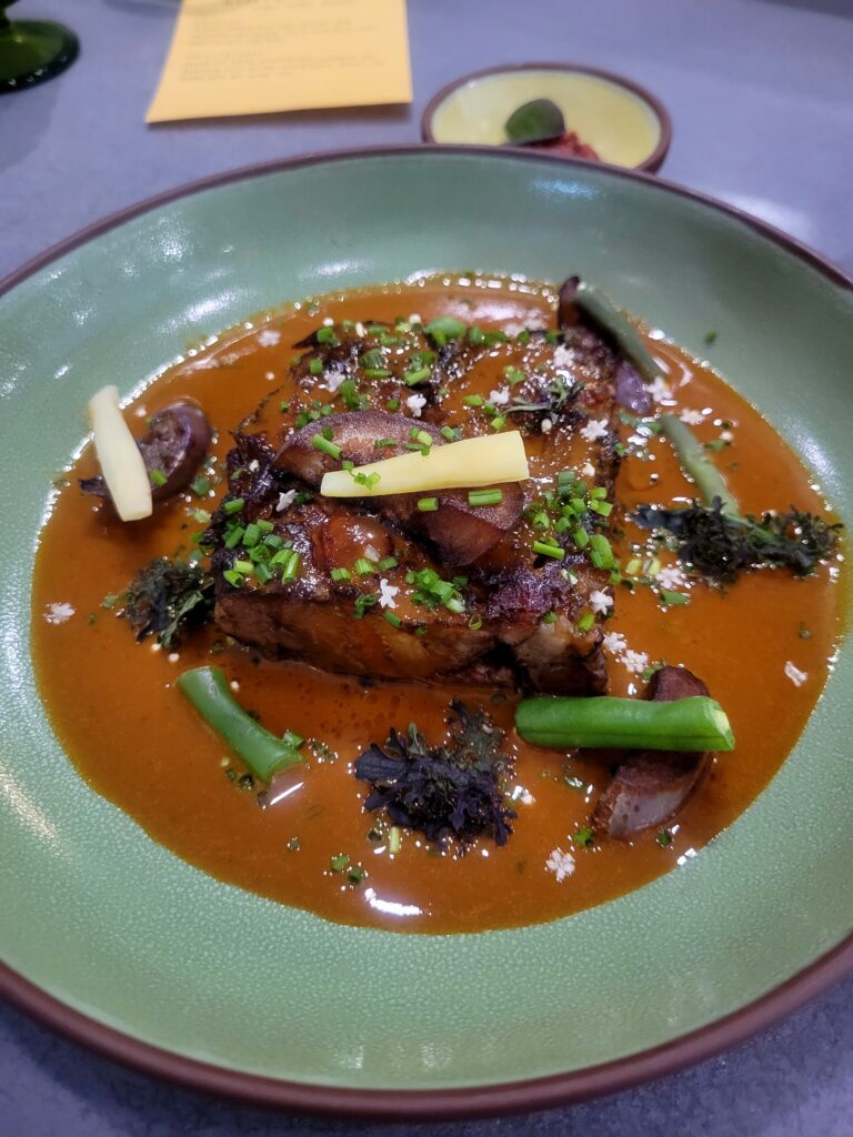 Kare-kare. Bit's of oxtail sits on a plate with a peanut sauce. There's broccolini, string beans and alliums scattered throughout the dish.